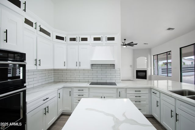 kitchen with custom exhaust hood, white cabinets, light stone counters, and black appliances