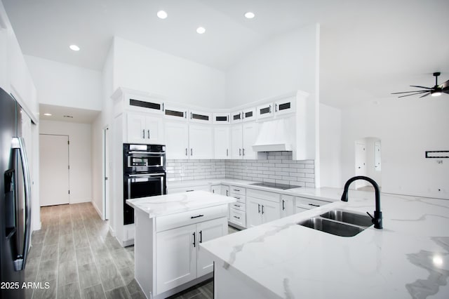 kitchen featuring light stone counters, sink, a center island, and premium range hood