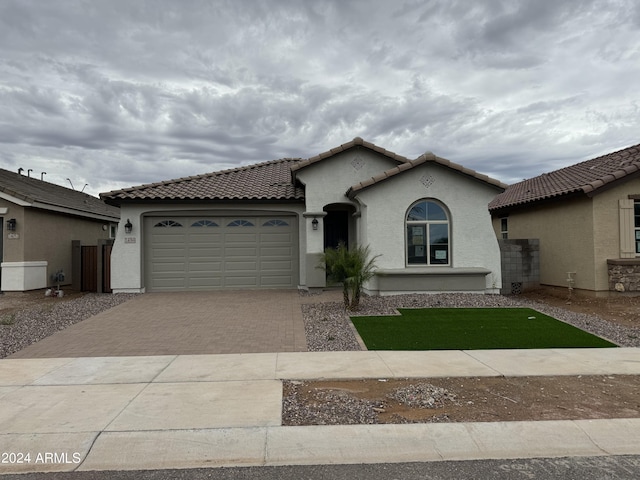 mediterranean / spanish home with a garage, decorative driveway, a tile roof, and stucco siding