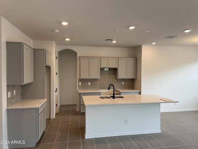 kitchen featuring an island with sink, tasteful backsplash, gray cabinets, sink, and a notable chandelier