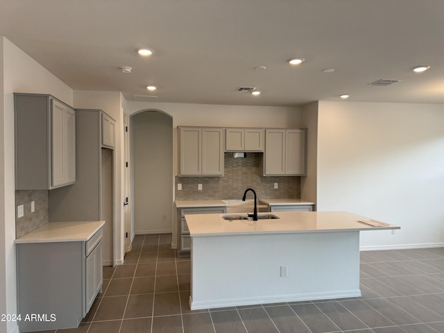 kitchen featuring arched walkways, visible vents, gray cabinetry, a sink, and dark tile patterned floors