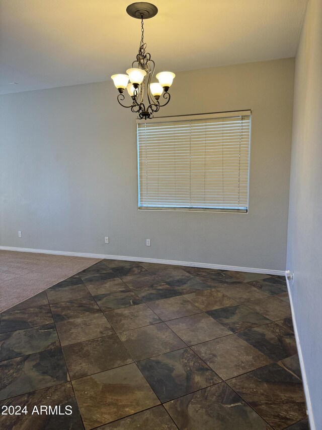 empty room with a chandelier and dark colored carpet