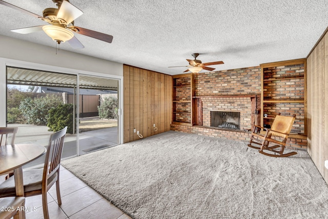 carpeted living room featuring ceiling fan, a textured ceiling, a brick fireplace, and wood walls