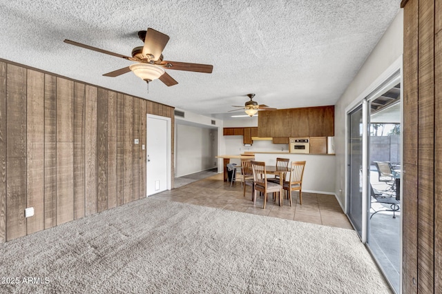 dining space with wooden walls, light tile patterned floors, visible vents, a textured ceiling, and light colored carpet