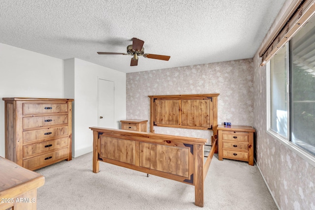 bedroom featuring wallpapered walls, ceiling fan, light colored carpet, and a textured ceiling