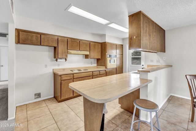 kitchen featuring a peninsula, white appliances, light countertops, and under cabinet range hood