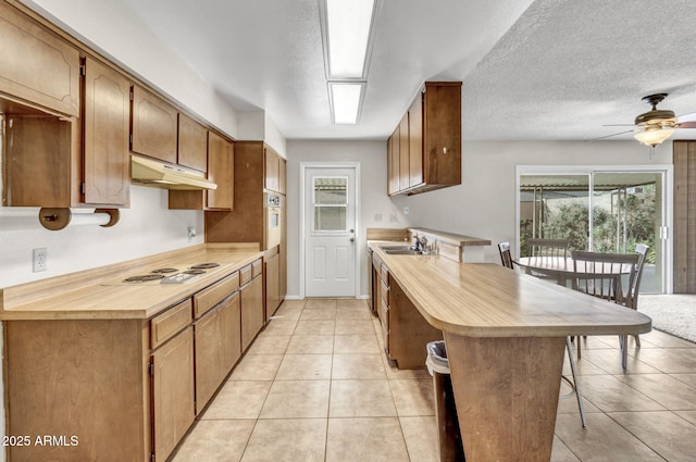 kitchen featuring white appliances, a breakfast bar, a peninsula, under cabinet range hood, and a textured ceiling