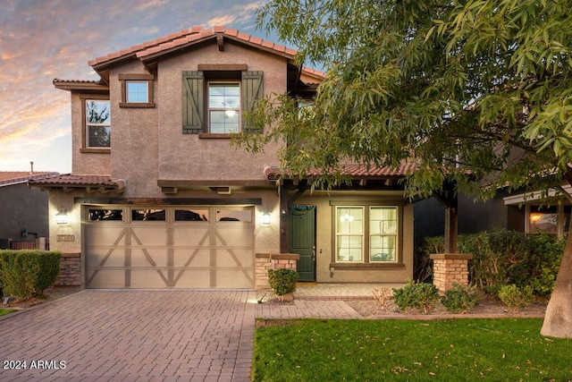 mediterranean / spanish-style house with an attached garage, stone siding, decorative driveway, and stucco siding