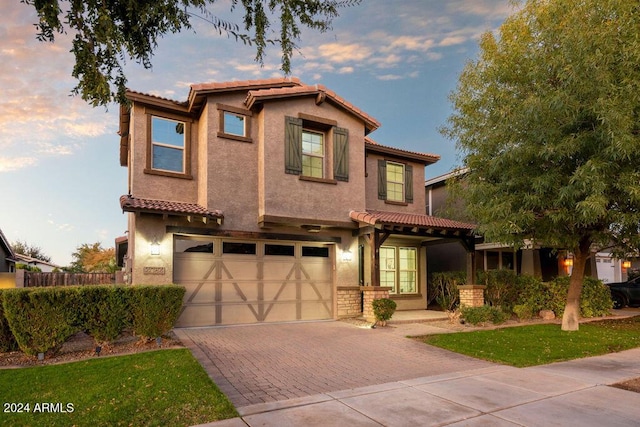 mediterranean / spanish-style home featuring a garage, decorative driveway, a tiled roof, and stucco siding