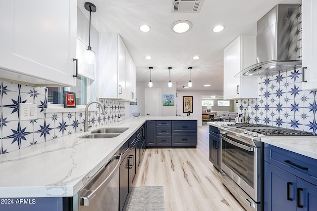 kitchen with white cabinets, sink, wall chimney range hood, and decorative light fixtures