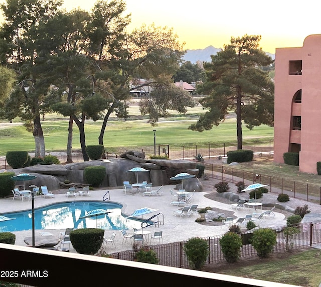 pool at dusk with fence, a lawn, and a patio area