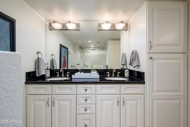 bathroom featuring a shower stall, double vanity, and a sink