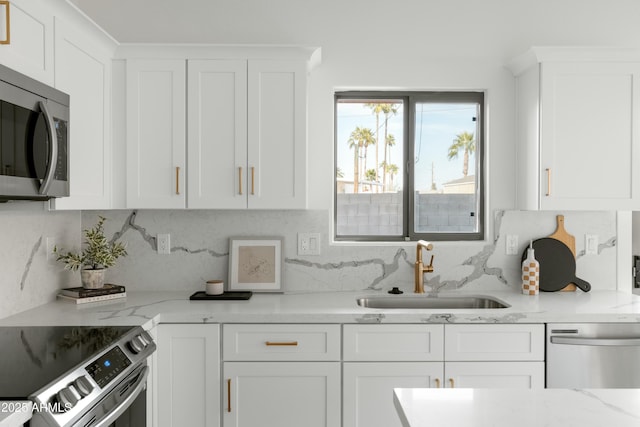 kitchen featuring appliances with stainless steel finishes, white cabinetry, sink, backsplash, and light stone counters