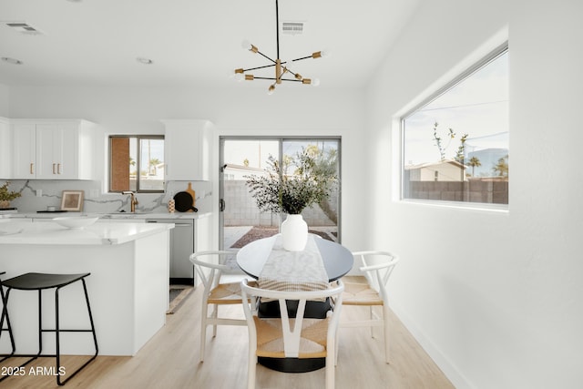 dining area featuring sink, a healthy amount of sunlight, light hardwood / wood-style flooring, and a chandelier