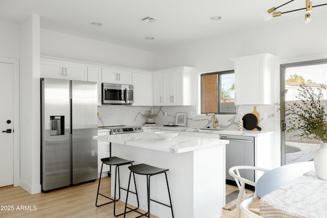 kitchen featuring light hardwood / wood-style flooring, white cabinetry, light stone countertops, a center island, and stainless steel appliances