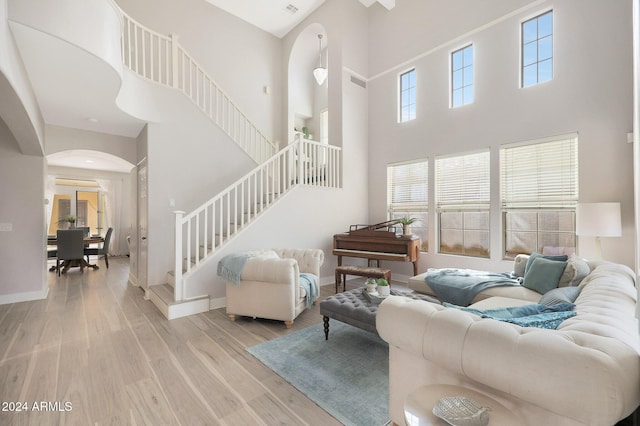 living room featuring light wood-type flooring, a towering ceiling, and a healthy amount of sunlight