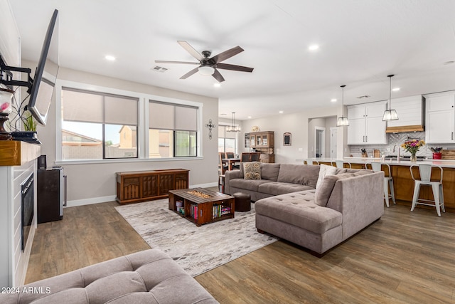 living room with ceiling fan with notable chandelier, sink, a fireplace, and hardwood / wood-style floors