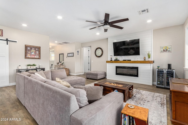 living room featuring a barn door, a large fireplace, light hardwood / wood-style floors, ceiling fan, and wine cooler