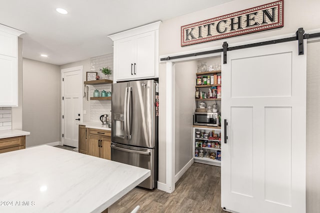 kitchen with appliances with stainless steel finishes, light wood-type flooring, a barn door, backsplash, and white cabinetry