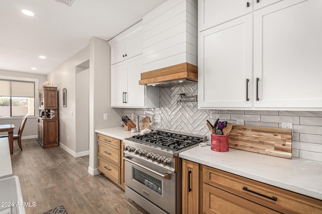 kitchen with hardwood / wood-style floors, tasteful backsplash, high end stainless steel range oven, premium range hood, and white cabinetry