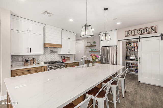 kitchen with a large island with sink, stainless steel appliances, light stone countertops, a barn door, and white cabinetry