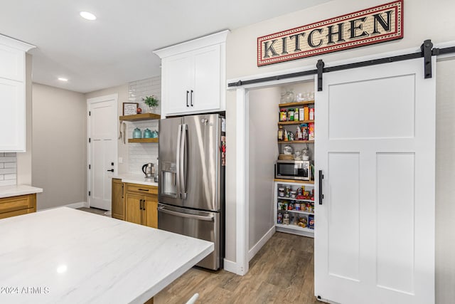 kitchen with decorative backsplash, appliances with stainless steel finishes, white cabinetry, a barn door, and light hardwood / wood-style floors