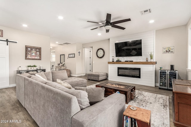 living room featuring hardwood / wood-style floors, beverage cooler, a large fireplace, ceiling fan, and a barn door