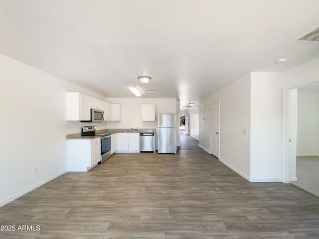 kitchen with wood finished floors, baseboards, white cabinets, a sink, and appliances with stainless steel finishes