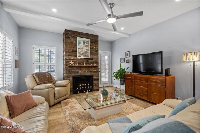 living room featuring beam ceiling, ceiling fan, a large fireplace, and light hardwood / wood-style floors