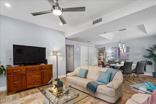 living room featuring light wood-type flooring, a tray ceiling, and ceiling fan with notable chandelier