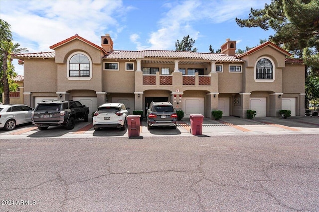 view of front of house with a garage, a tiled roof, a chimney, and stucco siding