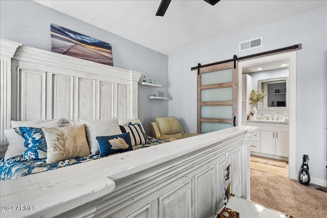 bedroom featuring a barn door, visible vents, ensuite bath, ceiling fan, and a sink