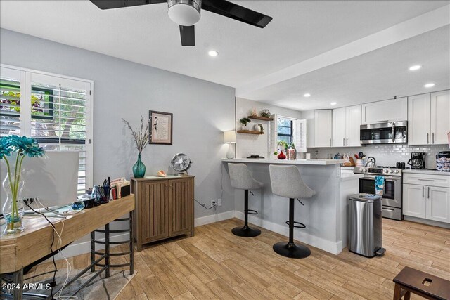 kitchen with appliances with stainless steel finishes, light hardwood / wood-style floors, a kitchen bar, kitchen peninsula, and white cabinets