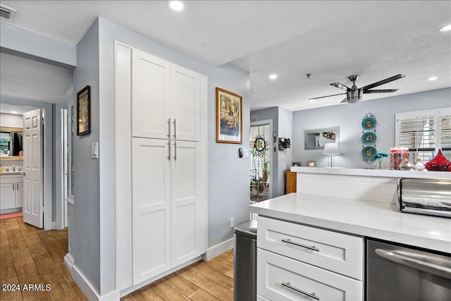 kitchen with light stone countertops, light hardwood / wood-style floors, stainless steel dishwasher, white cabinetry, and ceiling fan