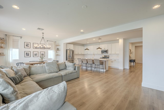 living room with visible vents, recessed lighting, light wood-style floors, an inviting chandelier, and baseboards