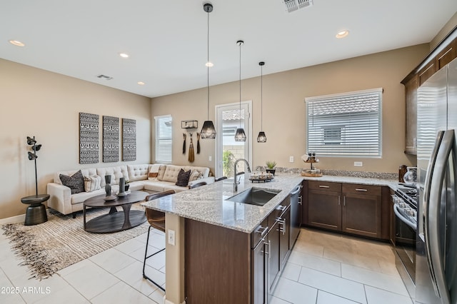 kitchen with a sink, dark brown cabinets, light tile patterned floors, appliances with stainless steel finishes, and open floor plan