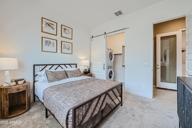 carpeted bedroom featuring stacked washer / dryer, a barn door, a walk in closet, and baseboards