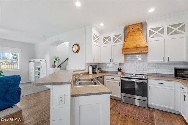 kitchen featuring sink, white cabinetry, stainless steel appliances, custom range hood, and kitchen peninsula