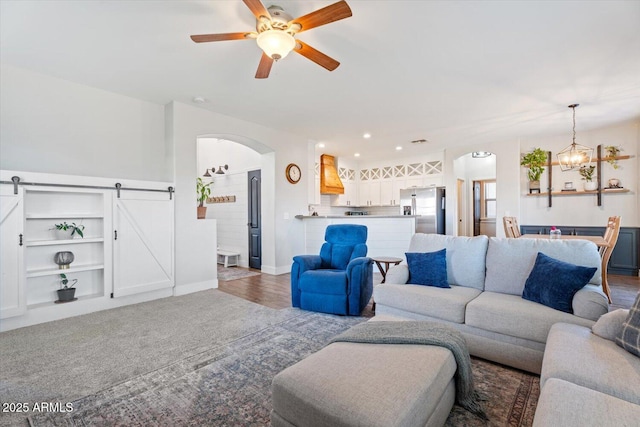 carpeted living room with a barn door and ceiling fan with notable chandelier