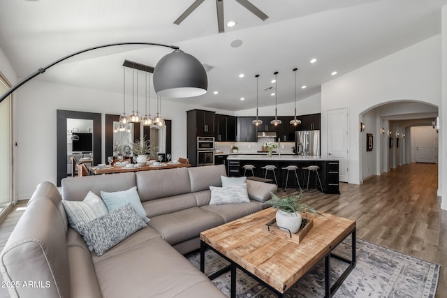 living room with lofted ceiling, ceiling fan with notable chandelier, and light hardwood / wood-style flooring