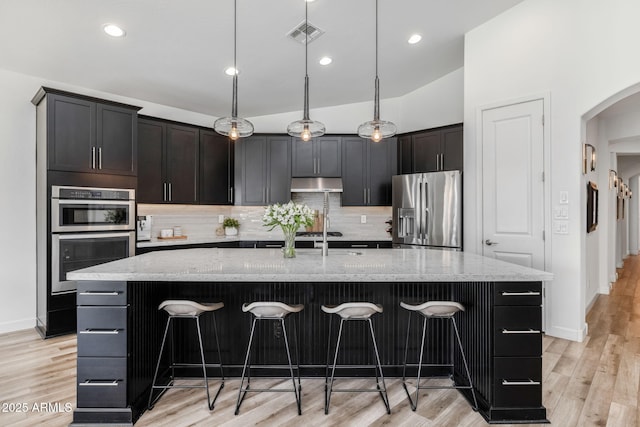 kitchen featuring appliances with stainless steel finishes, decorative light fixtures, a kitchen island with sink, and a breakfast bar area