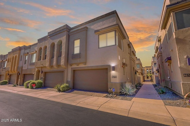 view of property featuring a residential view, an attached garage, driveway, and stucco siding