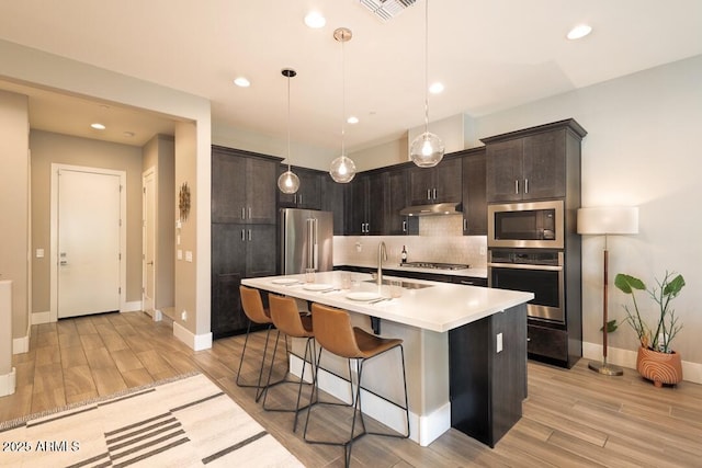 kitchen featuring decorative backsplash, a kitchen breakfast bar, a sink, light wood-style flooring, and appliances with stainless steel finishes