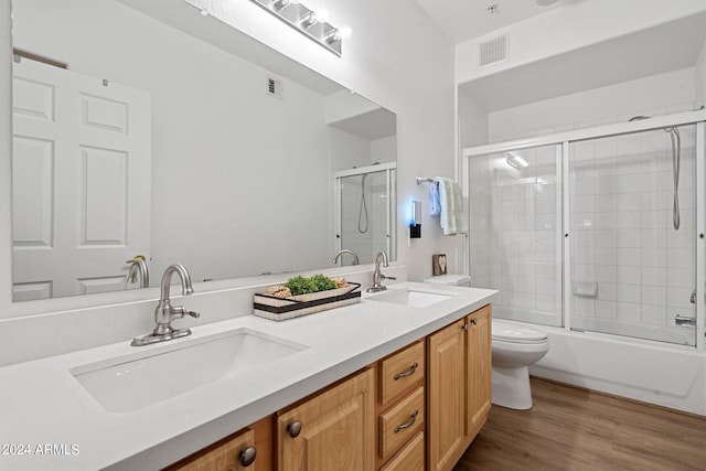 full bathroom with hardwood / wood-style floors, bath / shower combo with glass door, vanity, and toilet