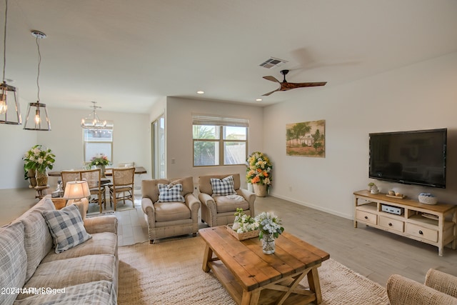 living room featuring ceiling fan with notable chandelier and light wood-type flooring