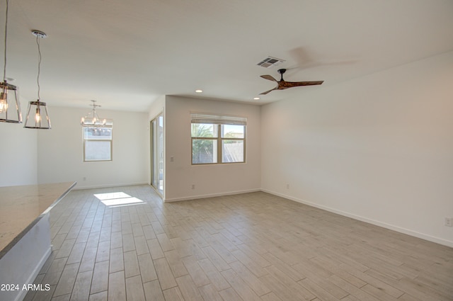 unfurnished living room with ceiling fan with notable chandelier and light wood-type flooring