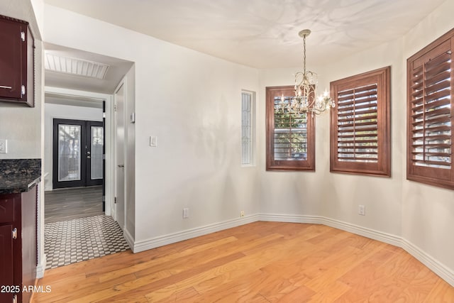 unfurnished dining area featuring light wood-type flooring, a notable chandelier, and french doors