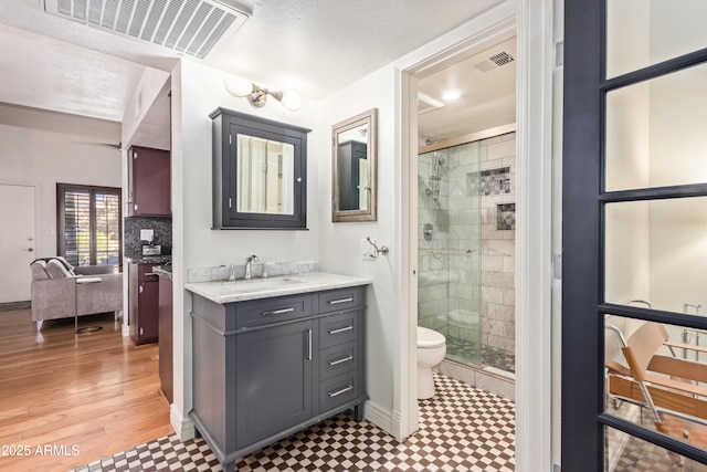 bathroom with a shower with door, a textured ceiling, toilet, vanity, and decorative backsplash