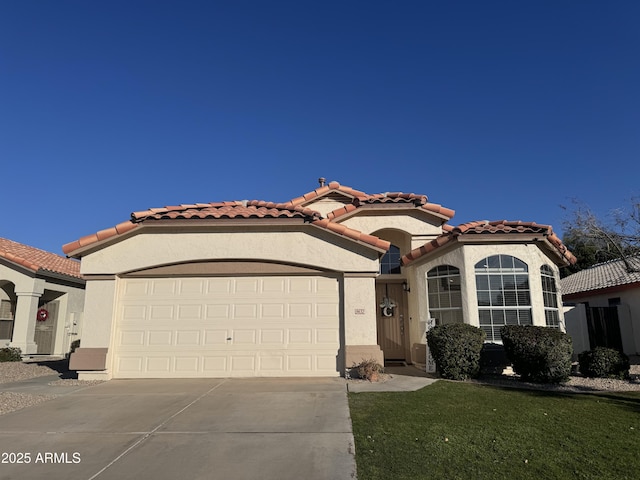 mediterranean / spanish house featuring a tile roof, stucco siding, a front yard, a garage, and driveway