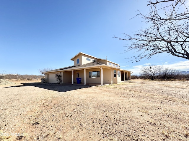 view of front of property with an attached garage, dirt driveway, and stucco siding